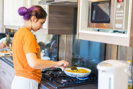 The girl prepares food. Woman warms up the dinner on the stove. Cooking at home. Gas stove. The girl in the kitchen.の写真素材