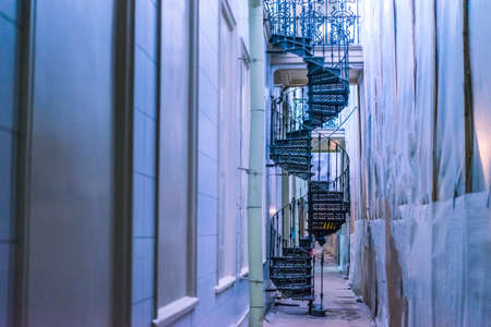 Spiral staircase between buildings. A metal ventilated staircase. A black staircase facing the building.の写真素材