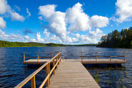 Wooden berth. Pier on the river. View of the river pier on a summer day. A wooden bridge leads to the water. Pier for swimming. Swimming season. Summer rest near the water.の写真素材