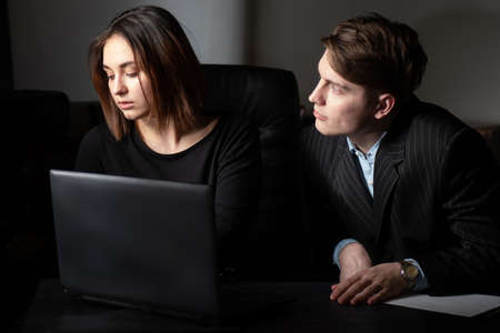 Flirt at work. The love relationship of colleagues. Fall in love with a colleague. Harassment at work. A man pesters his colleague a woman. A man gives sexual signs.の写真素材