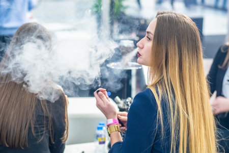 Woman smokes a hookah. Smoke. The girl releases tobacco smoke. Smoking accessories. Tabaka. Hookah Club Show. Exhibition of hookahs. 9.3.2019. Russia. Saint Petersburgのeditorial素材