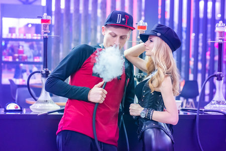 The girl and the guy smoke hookah. Smoke. A man produces smoke. Smoking accessories. Tabaka. Hookah Club Show. Exhibition of hookahs. 9.3.2019. Russia. Saint Petersburgのeditorial素材