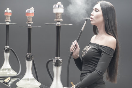 Woman smokes a hookah. Smoke. The girl tastes tobacco. Smoking accessories. Tabaka. Hookah Club Show. Exhibition of hookahs. 9.3.2019. Russia. Saint Petersburgのeditorial素材