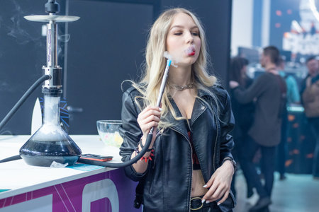 Woman smokes a hookah. Smoke. The girl tastes tobacco. Smoking accessories. Tabaka. Hookah Club Show. Exhibition of hookahs. 9.3.2019. Russia. Saint Petersburgのeditorial素材