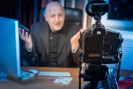 A businessman is recording a video. A man works in front of the camera. Businessman in a suit. Video blogger. Broadcast via the Internet. Businessman tells how to make money.の写真素材