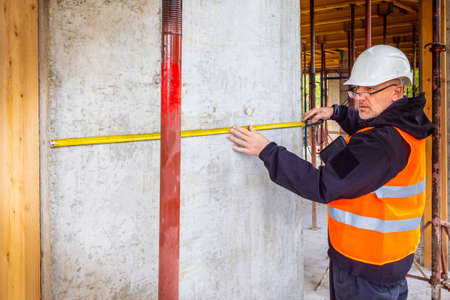 The builder verifies the data. Construction of the building. Control over the construction. Inspection. A man in a construction helmet. A man with a tape measure.の写真素材