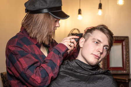 A girl with a clipper cutting a guy's hair. Men's haircut. Girl hairdresser.