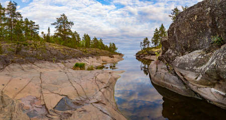 Rocky coast of the island. Wildlife panorama. Cove on the lake. Stones in the water. Spruce forest on the shore of the island. Islands in Lake Ladoga. Karelia. The nature of Russia. Ladoga lake.の写真素材
