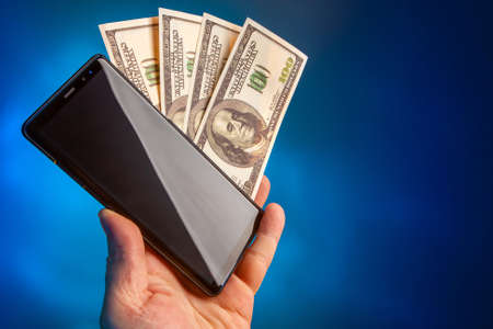 Mobile phone. Payment of cellular communication. Phone on the background of money. Dollars. Man's hand is holding a phone and dollars. The cost of mobile communications. Money transfer.の写真素材