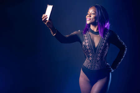 Selfie girl. A black woman in a bodysuit takes a photo of herself on the phone. Selfshot. A self-portrait photo. Photo for social networks. Narcissism.の写真素材