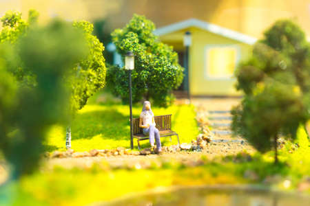 A woman is sitting on a bench near the house. Designing of low-rise buildings. The girl on the bench. The house is surrounded by trees.の写真素材