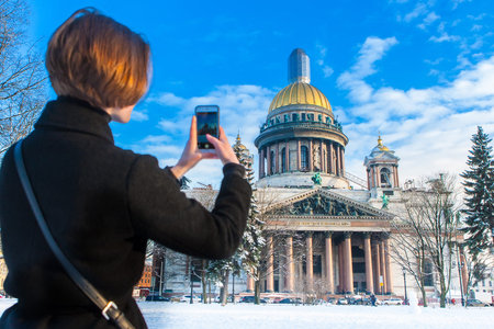 The girl takes pictures of the museums of St. Petersburg. Saint Isaac's Cathedral. Architecture of Russia. City in the snow. Saint Petersburg 03/20/2018のeditorial素材