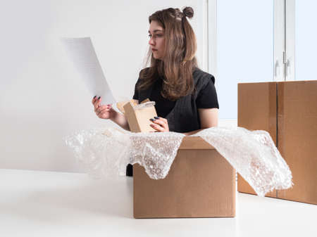 Online store. Dispatch of orders. A girl is packing goods for delivery. A woman formes the parcel. A packer with a bill of lading in her hands. Product packaging.の写真素材