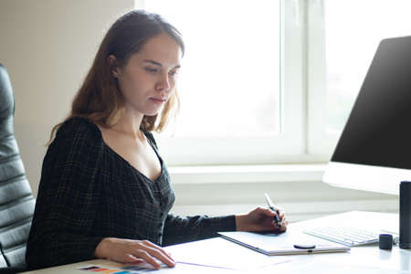 The girl works as a designer. The designer executes the project. A woman draws on a graphics tablet. Designer at work. The girl thinks over the design of her house.の写真素材