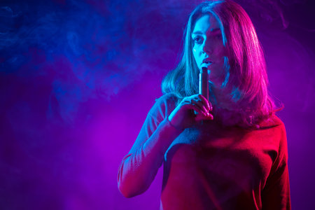 The girl holds the VAPE near her lips. The concept of vaping. A long-haired girl with a VAPE on a...