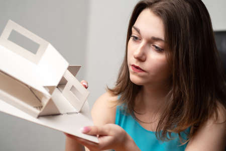 A young girl holds a model of an apartment in her hands. Dreams about your home. The dream apartment. Housing is a good choice. Real estate acquisition. Repairs in the apartment.の写真素材