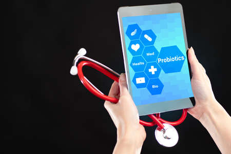 Probiotics advantages. Space for text. Hands with a tablet with a message about probiotics and a stethoscope. The concept of probiotics on a black background. Use of gram-positive bacteria in medicineの写真素材