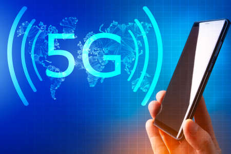 Creative 5G blue background. A man's hand holds the phone next to the 5g symbol. 5g logo on the background of the world map. Space for text. High-speed mobile Internet. New generation network.の写真素材
