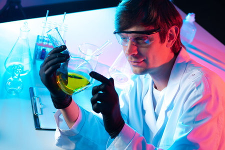A man examines a yellow chemical liquid in a flask. Checking the quality of raw materials. Chemical...