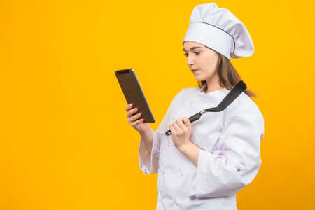 Cooking recipes. Cooking according to recipes. A girl in a chef's uniform looks at new recipes on a tablet. Cuisine of the world. National cooking.の写真素材