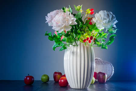 A bouquet of peonies and raspberries in a white vase. Autumn still life. Flowers and apples on the table. Bouquet of flowers and berries.の写真素材