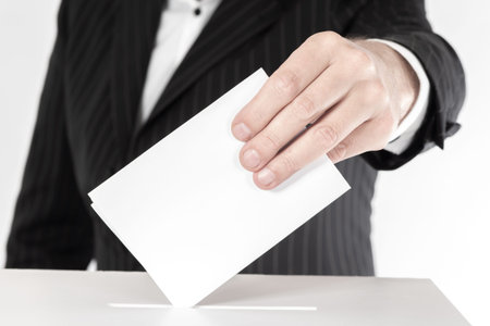 A man hand drops the ballot into the voting basket. Hand of a voter with a ballot close-up. The...