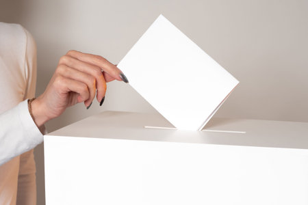 A woman drops a ballot into the ballot box. A woman votes in an election. The concept of elections....