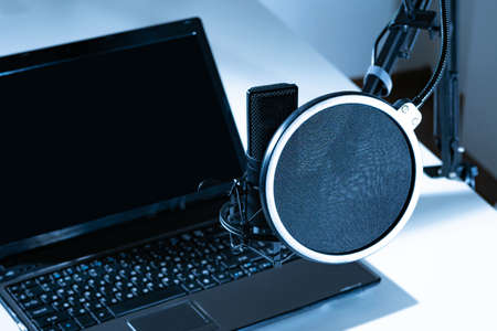 Laptop and microphone close-up. The usual set for voice work. Professional black microphone on a tripod. Black-and-white concept of recording.の写真素材