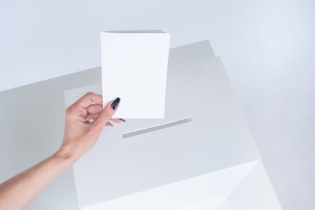 A woman hand drops a ballot into the ballot box. The concept of voting in elections in white. A...