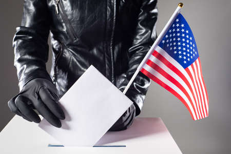 Voting in elections during the period of the pandemic coronavirus. An American woman puts a ballot in the voting basket with her hands in rubber gloves. US Presidential election.の写真素材