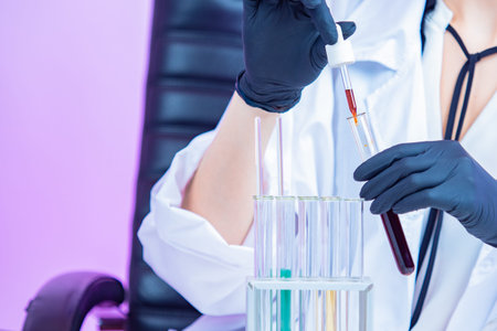 Hands of a chemist with a pipette and a test tube. Adding a reagent to the test chemical liquid....