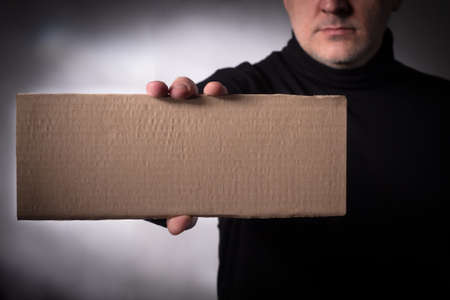 A man in a black sweater is holding a cardboard sign. Space for text. Making demands. Important information message. A cardboard poster with a place for the inscription in the hands of a man.の写真素材