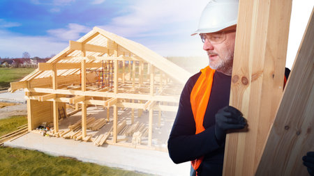 Construction of wooden houses. Joinery. Carpenter on the background of a cottage under construction. A man in a white helmet with planks in his hands at a construction site.の写真素材