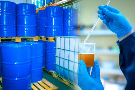 Chemical research at the enterprise. A chemist holds a container of chemical liquid against a background of blue barrels. Fuel quality check. Chemist in the laboratory of the enterprise.の写真素材