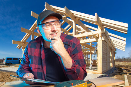 A carpenter working in construction. Carpenter on the background of the frame of a new house. A man...