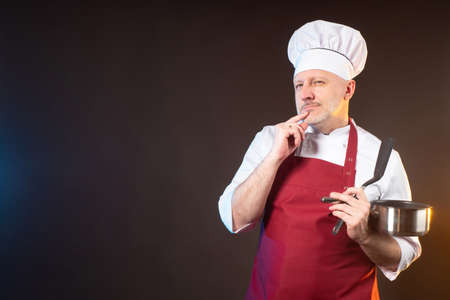 Creativity in cooking. Brooding chef with a pot in his hands. The chef comes up with a new recipe. Cook with a pot in his hands on a brown background. Space for text.の写真素材