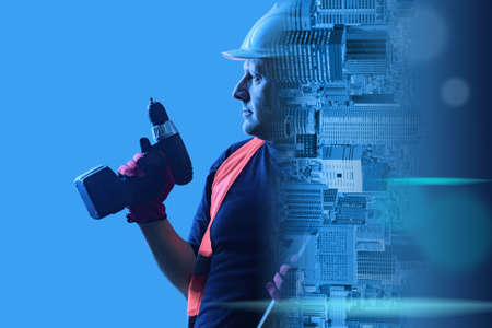 Construction and repair. A Builder with a battery-powered screwdriver in his hand merges with the panorama of the city. A man in a white hard hat and reflective vest on a blue background.の写真素材