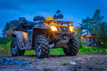 A dirty ATV stands next to the cottage in the evening. Off-road riding on ATV. Active sports....