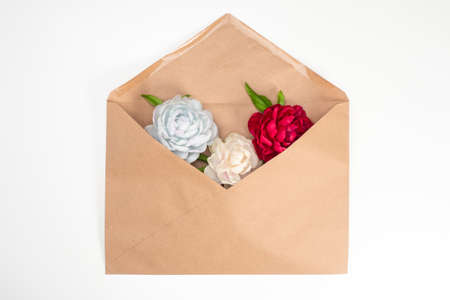 The concept of greetings. Flowers in a brown envelope on a white background. The envelope is filled with beautiful flowers. Love letter. Romance.の写真素材