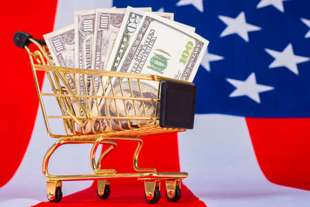 The shopping cart is filled with dollars. A shopping cart with money stands on an American flag. Trade in the United States. American online stores.の写真素材