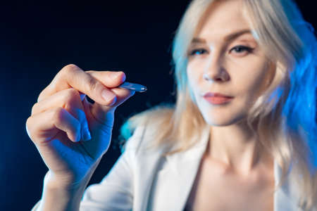 Beautiful blonde with a stylus in her hands. The girl brings the stylus to the glass control panel. Modern technology. Touchscreen. A woman with a stylus in her hands.の写真素材