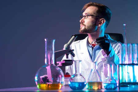 Portrait of a chemist on the background of a microscope and glassware. A bearded man conducts experiments with chemical liquids. Chemist on a gray background. Chemical laboratory equipment.の写真素材