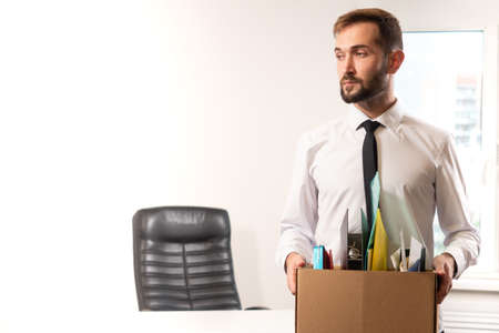 Sad dismissed man. A man is holding a box of office supplies. Dismissal from work. Reduction of the company staff. Bankruptcy of the company. Problem of job loss. Place for text.の写真素材