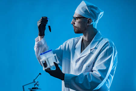 A laboratory assistant holds test tubes with blood samples. All types of laboratory tests. Research of biological fluids. Doctor with blood samples on a blue background. Laboratory diagnostics.の写真素材
