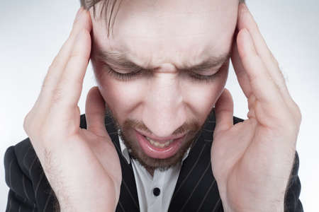 Portrait of a man with a frowning forehead, holding his head. Headache. Migraine. A person can't cope with problems. The man is in shock. A shaken man.の写真素材