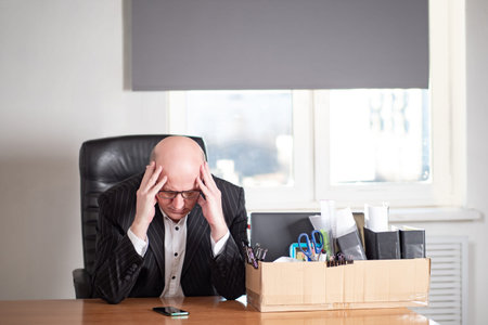A man is sitting in his office next to a box of office supplies. Dismissal. Job loss. Ruin of the...