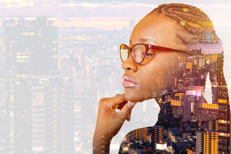 A dark-skinned girl merges with the evening city. An African-American woman reflects on the background of the city. Dark-skinned model with braids.の写真素材
