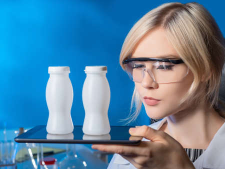 Drinks with probiotics. Laboratory testing of food products. A female lab assistant holds a tablet and bottles with a drink. Fortified foods. Dairy products with probiotics.の写真素材