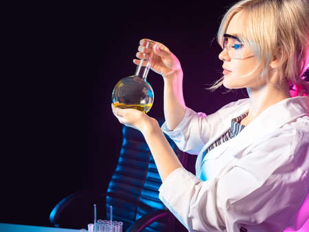 Chemist with a flask in her hands. Study of chemistry. A chemistry teacher demonstrates an experiment. Practical classes in chemistry. The girl is holding a flask with a yellow chemical liquid.の写真素材