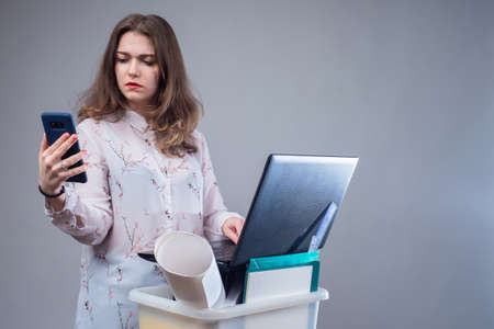 Job search. The dismissed employee is looking for a new job. A woman responds to vacancies. Job loss. A girl with a box of office supplies, a smartphone and a laptop.の写真素材